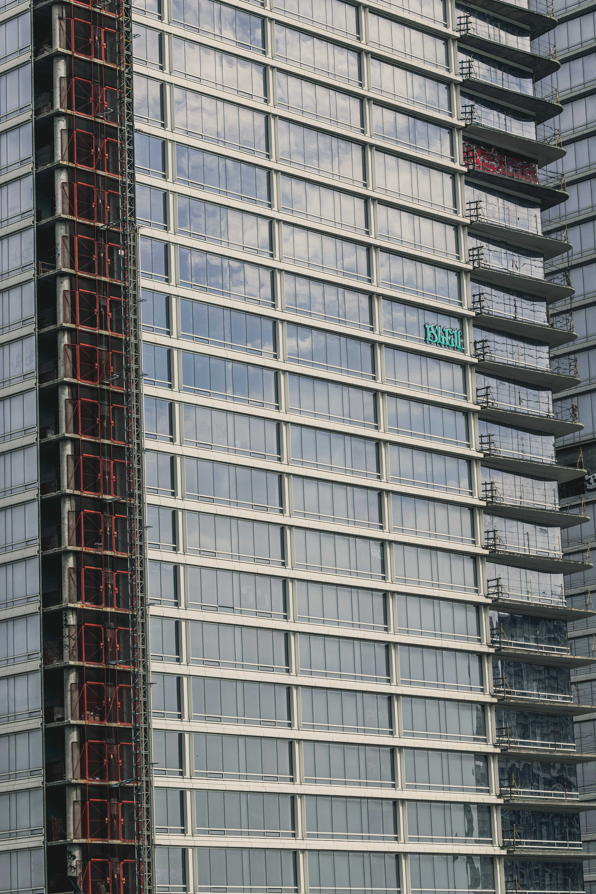 A small turquoise tag interrupts a wide grid of pale windows beside a rust-red construction shaft