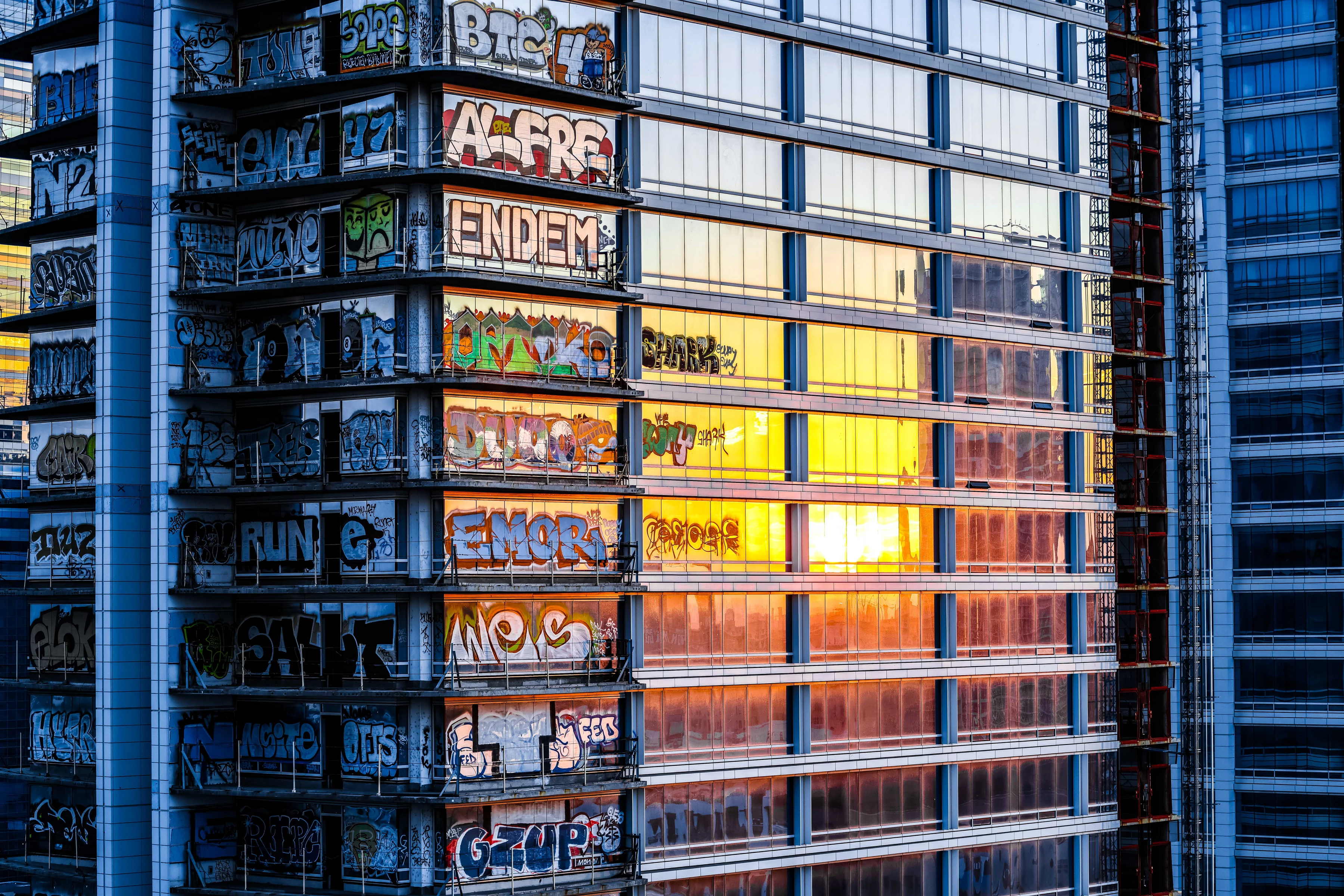 Sunrise reflected in glass beside a shadowed column of painted balconies